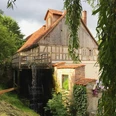 Mühlrad Elbrinxen Historische Wassermühle mit sichtbarem Mühlrad und Fachwerkhaus, umgeben von üppigem Grün.