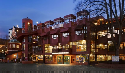 Rotes, modernes Gebäude mit vielen Fenstern und Treppen in nächtlicher Beleuchtung.