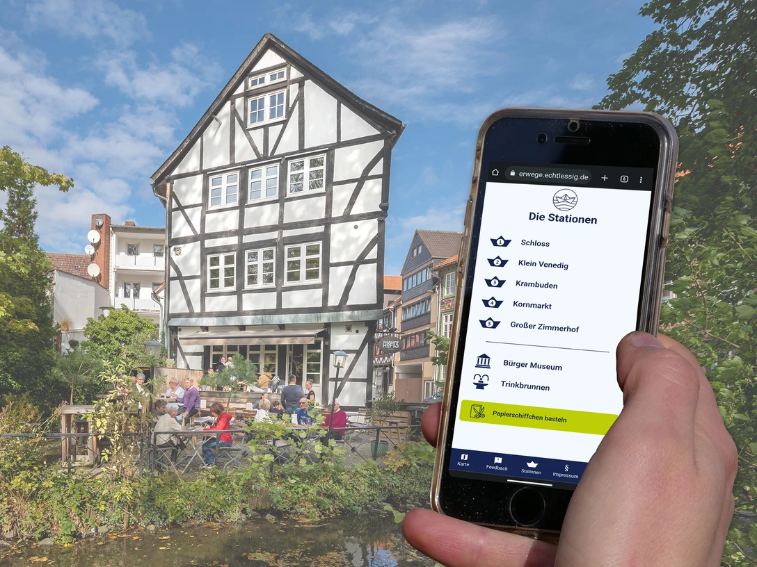 Handydisplay zeigt Stationsübersicht, Fachwerkhaus mit Terrasse am Wasser