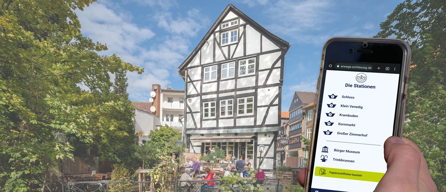 Handydisplay zeigt Stationsübersicht, Fachwerkhaus mit Terrasse am Wasser