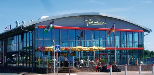f-hrhause-terrasse-mit-logo Das Fährhaus am Emder Außenhafen: Modernes Gebäude mit bunten Sonnenschirmen.