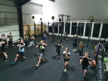 Crossfit Kettlebell Eine Gruppe von Menschen trainiert in einem Fitnessstudio mit Kettlebells auf schwarzen Matten.