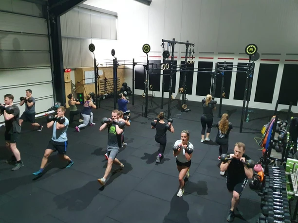 Crossfit Kettlebell Eine Gruppe von Menschen trainiert in einem Fitnessstudio mit Kettlebells auf schwarzen Matten.