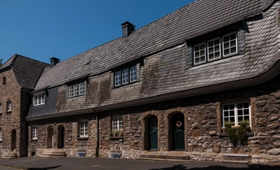 Das Bild zeigt eine historische Reihenhausfassade aus Stein mit Schieferdach und weißen Fenstern.