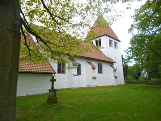 Weiße Kirche mit rotem Ziegeldach in grüner, ruhiger Umgebung, von Bäumen umgeben.