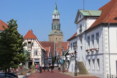 Quakenbrück Marktplatz Straßenansicht in einem historischen Stadtkern mit Fachwerkhäusern und Kirchturm im Hintergrund.