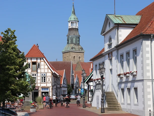 Quakenbrück Marktplatz Straßenansicht in einem historischen Stadtkern mit Fachwerkhäusern und Kirchturm im Hintergrund.