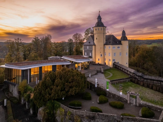 Schloss Homburg <p>Schloss Homburg bei Sonnenuntergang, umgeben von Bäumen und einem modernen Anbau, im Herbst.</p>