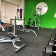 fitplus-wiefelstede-freihantel Freihantelbereich im modernen Fitnessstudio: Bänke, Hanteln und ein heller, grüner Raum.