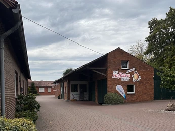 Hofladen Denker Ein Hofladen aus rotem Backstein mit Werbeschildern und einer kleinen Terrasse vor dem Eingang.