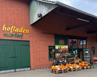 Hofladen Niemeyer Hofladen mit Backsteinfassade und grünem Holztor, dekoriert mit Kürbissen und Blumenschildern.