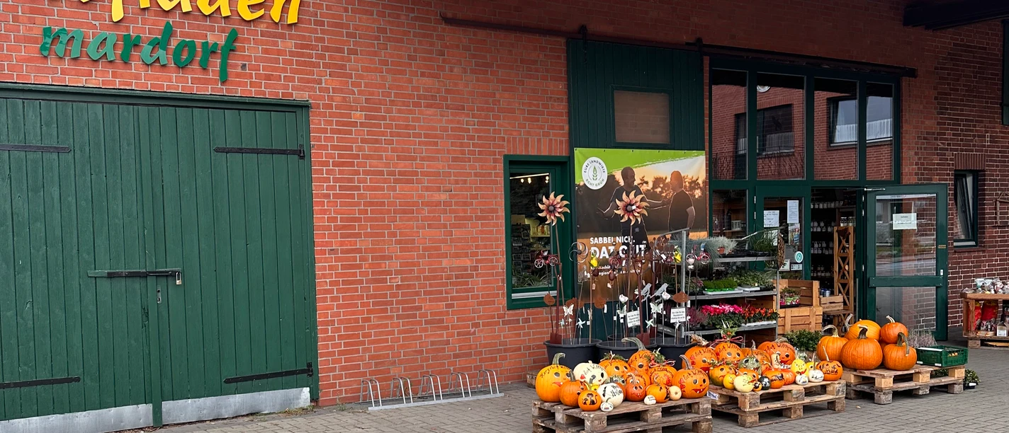 Hofladen Niemeyer Hofladen mit Backsteinfassade und grünem Holztor, dekoriert mit Kürbissen und Blumenschildern.