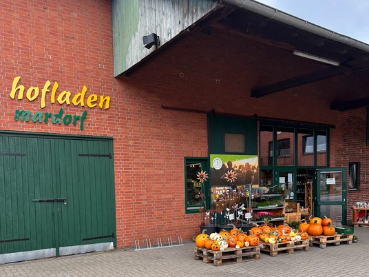 Hofladen Niemeyer Hofladen mit Backsteinfassade und grünem Holztor, dekoriert mit Kürbissen und Blumenschildern.