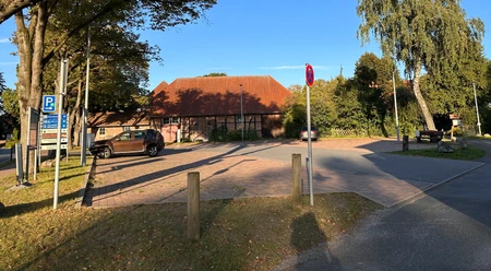 Parkplatz Kleiner Brink Parkplatz mit Pflastersteinen, umrahmt von Bäumen und einem Gebäude mit rotem Ziegeldach.