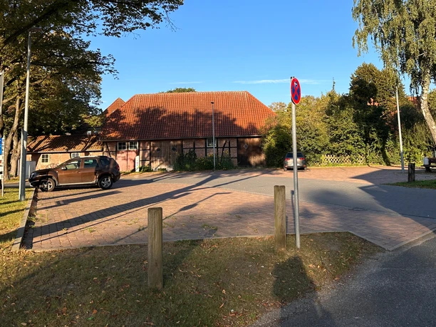 Parkplatz Kleiner Brink Parkplatz mit Pflastersteinen, umrahmt von Bäumen und einem Gebäude mit rotem Ziegeldach.