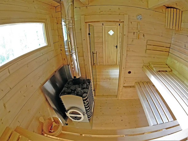 Forsthaus Bielatal Finnische Blockhaussauna Holzsauna mit Bänken, einem Ofen mit Steinen und einem Eimer mit Kelle; warmes, einladendes Ambiente.