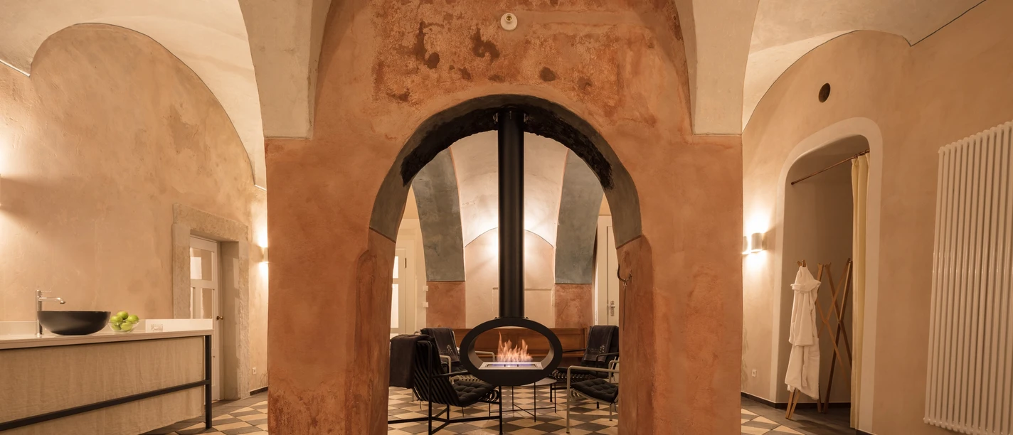Gezellige kamer met gewelfde plafonds en een centrale open haard omringd door fauteuils. Warme verlichting en een ontspannen sfeer.