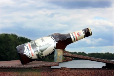 Papenburger Landbier Braune Bierflasche Papenburger Landbier auf rostigem Metall vor bewölktem Himmel und Wald.