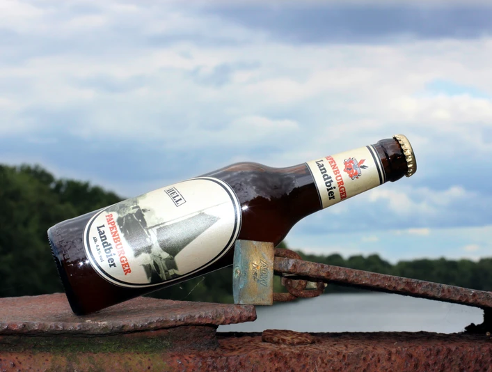 Papenburger Landbier Braune Bierflasche Papenburger Landbier auf rostigem Metall vor bewölktem Himmel und Wald.