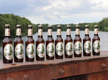 Papenburger Landbier Reihe Papenburger Landbier-Flaschen auf rostigem Geländer vor Fluss und grüner Baumkulisse
