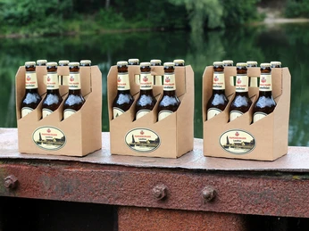 Papenburger Landbier Drei Sixpacks Papenburger Landbier auf rostiger Metallkante vor grünem Seeufer arrangiert.