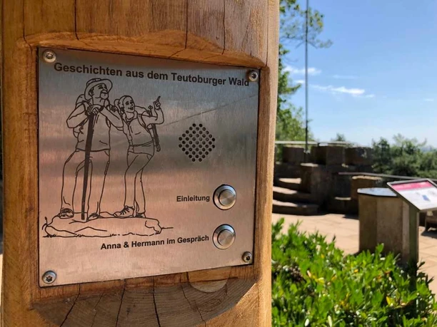 Hörstation Anna & Hermann in Hörstel Hörstation im Teutoburger Wald mit Schildern für Audio-Einleitung, umgeben von Bäumen und Natur.