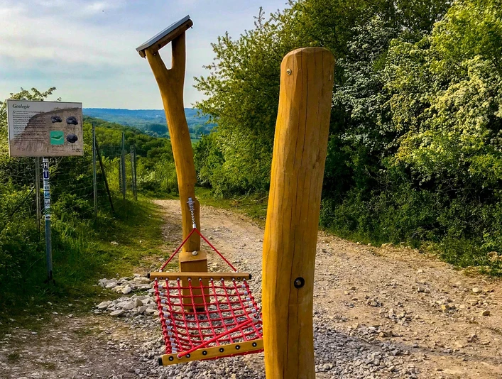 Hörstation 05 am Dyckerhoff Steinbruch Hörstation im Dyckerhoff Steinbruch, umgeben von Bäumen, mit Info-Tafel und Seilnetz zum Entspannen.