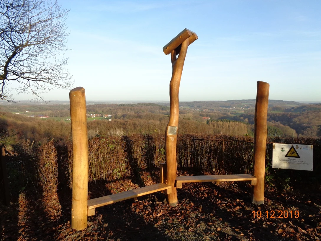 Hörstation Anna & Hermann in Lienen Skulptur aus Holzstämmen mit Hörrohren auf einem Hügel, weite Aussicht über bewaldetes Umland.