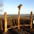 Hörstation Anna & Hermann in Lienen Skulptur aus Holzstämmen mit Hörrohren auf einem Hügel, weite Aussicht über bewaldetes Umland.