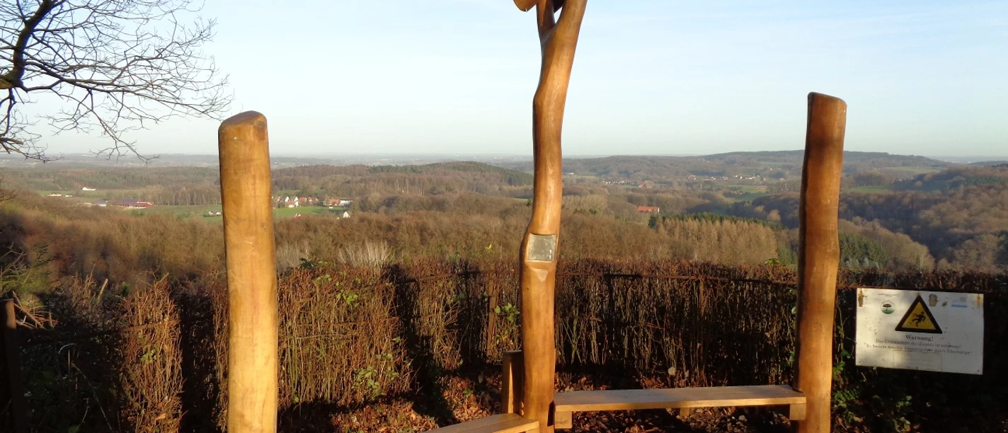 Hörstation Anna & Hermann in Lienen Skulptur aus Holzstämmen mit Hörrohren auf einem Hügel, weite Aussicht über bewaldetes Umland.