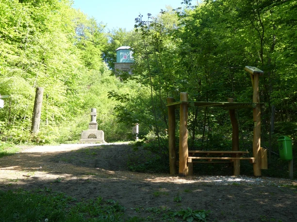 Hörstation 11 in Halle Westfalen Ein Weg führt durch einen grünen Wald zu einer hölzernen Hörstation und einem steinernen Denkmal.