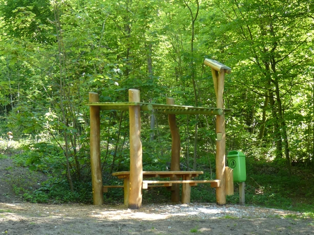 Hörstation Anna & Hermann in Halle Westfalen Hörstation im Wald mit Holztisch und Lärmdach, umgeben von üppigem Grün, lädt zur Pausengestaltung ein.