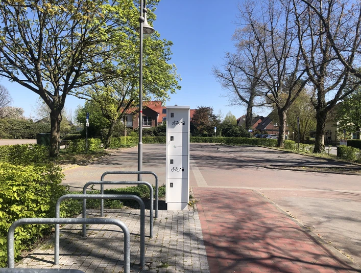 eBike Ladestation am Kögel-Willms-Platz Fahrradständer und Aufbewahrungsboxen an einem ruhigen Platz mit Bäumen und blauem Himmel