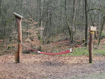 Hörstation Hermannshöhen in Lage-Hörste Eine rote Hängematte aus Netzmaterial ist zwischen zwei Holzpfosten im bewaldeten Gebiet gespannt.