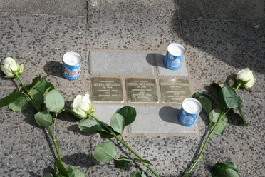 Stolpersteine Drei Stolpersteine mit weißen Rosen und brennenden Kerzen zum Gedenken an NS-Opfer.