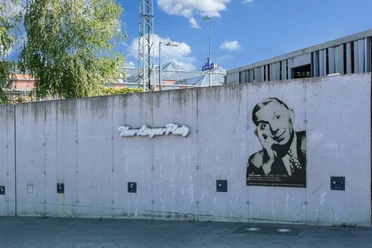 Theo Lingen Graue Betonwand mit Porträt von Theo Lingen und Schriftzug Theo-Lingen-Platz bei blauem Himmel