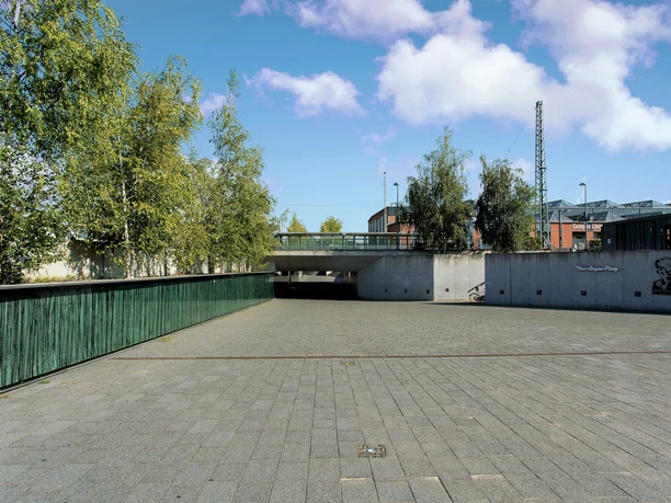 Theo Lingen Moderner Platz mit Bäumen, Betonwänden und Wandkunst von Theo Lingen unter blauem Himmel