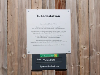 ladestation-park-der-gaerten1.jpg Hinweisschild einer E-Ladestation im Park der Gärten mit Informationen zur Nutzung und Spendenbox.