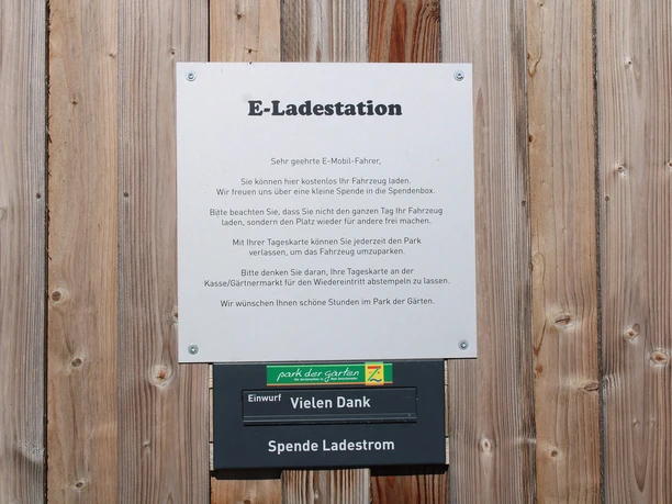 ladestation-park-der-gaerten1.jpg Hinweisschild einer E-Ladestation im Park der Gärten mit Informationen zur Nutzung und Spendenbox.