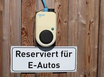 ladestation-park-der-gaerten2.jpg Auf Holz angebrachtes Schild mit Aufschrift "Reserviert für E-Autos" unter einer E-Ladestation.