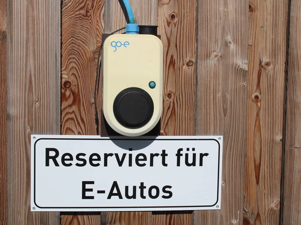 ladestation-park-der-gaerten2.jpg Auf Holz angebrachtes Schild mit Aufschrift "Reserviert für E-Autos" unter einer E-Ladestation.