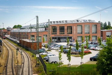 Campus Lingen Backsteingebäude des Campus Lingen mit Glasdach, angrenzenden Bahngleisen und Parkplatz.