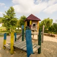 Abenteuerspielplatz im Emmerauenpark Spielplatz im Emmerauenpark mit Holzturm, Rutsche, bunten Holzpfosten, Sandboden und Bäumen.