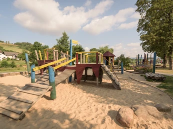 Kinderspielplatz Emmerauenpark Abenteuerlust auf Holzspielgeräten im Emmerauenpark mit Sandfläche und grüner Umgebung.