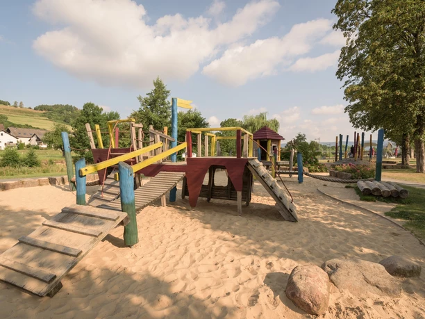 Kinderspielplatz Emmerauenpark Abenteuerlust auf Holzspielgeräten im Emmerauenpark mit Sandfläche und grüner Umgebung.