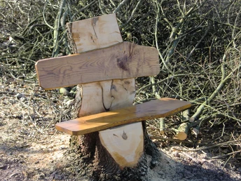 Blick nach Meilborssen Holzbank ohne Lehne, gefertigt aus einem Baumstamm, umgeben von kahlen Ästen auf einem erdigen Boden.