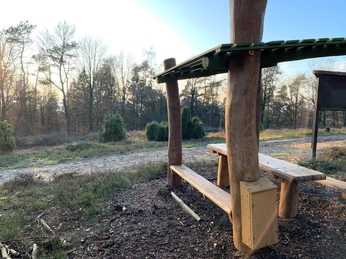 Hörstation Steinhagen mit Blick nzum Hermannsweg Holzbänke unter einem schützenden Dach, umgeben von Wald, bieten Rastmöglichkeit am Hermannsweg.
