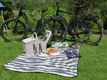 img_0403 Zwei Fahrräder stehen auf einer Wiese, davor liegt eine Picknickdecke mit Essenskorb und Snacks.