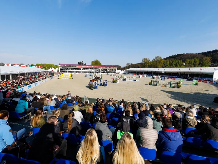 Hof Kasselmann_Springplatz_CC_Familie Kasselmann Ein Pferdesport-Event mit vielen Zuschauern auf Tribünen, Reiter springen über Hindernisse.