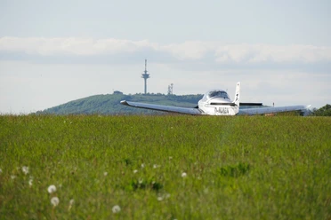 Flugplatz am Räuschenberg mit Köterberg im Hintergrund Ein kleines Flugzeug steht auf einer grünen Wiese mit dem bewaldeten Köterberg und einem Funkturm im Hintergrund.
